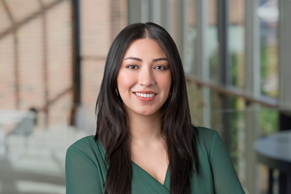 A headshot of Ana Espinal with a blurred out background of windows and a brick wall.